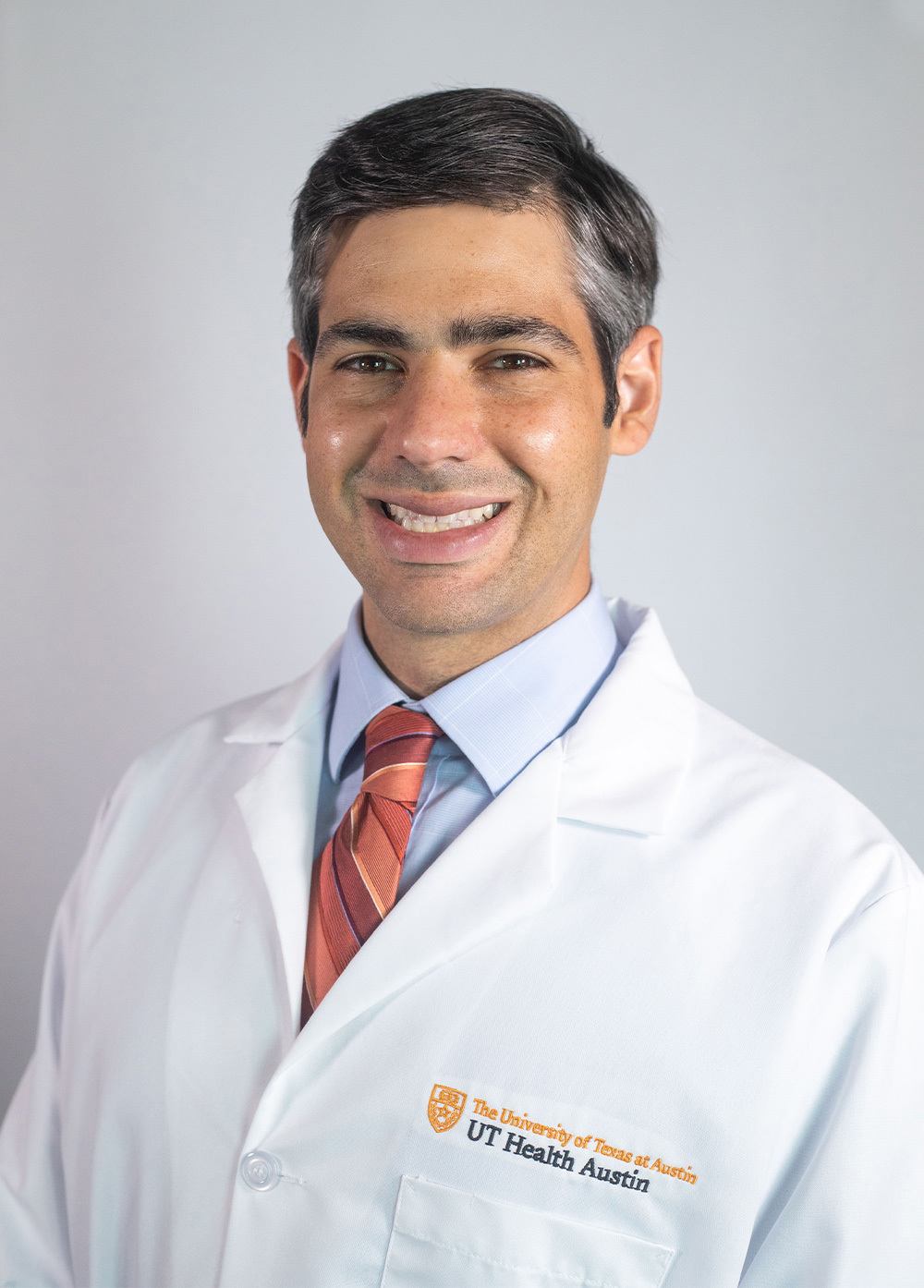 Internal medicine specialist Scott Selinger, MD, FACP, wearing a white coat and smiling in front of a white backdrop.