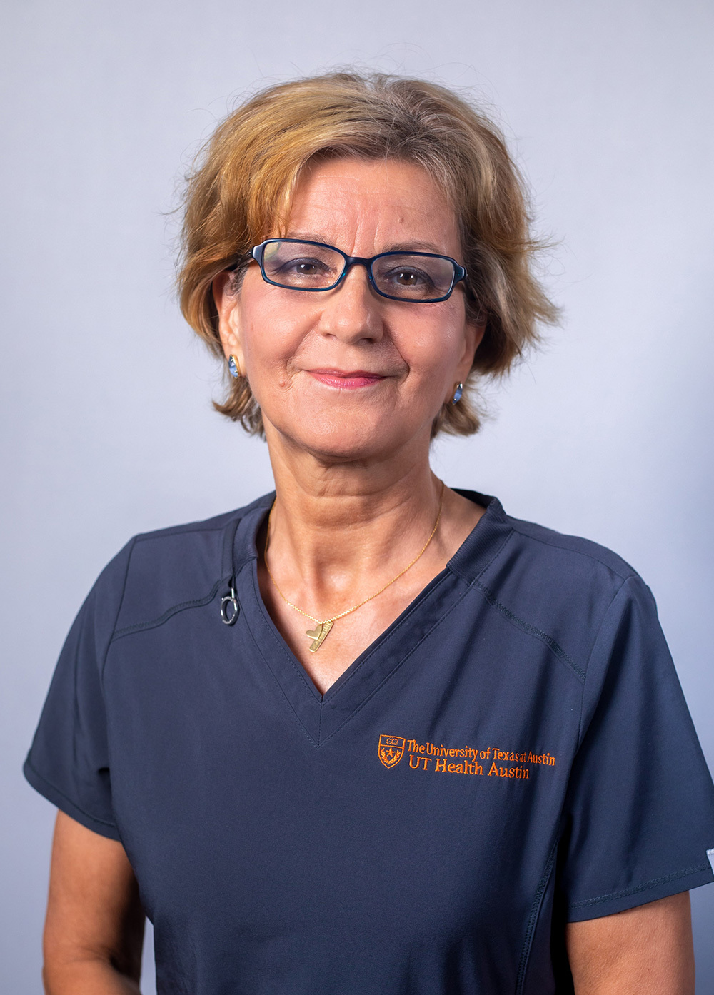 Stela Olteanu wearing dark scrubs and smiling in front of a white backdrop.