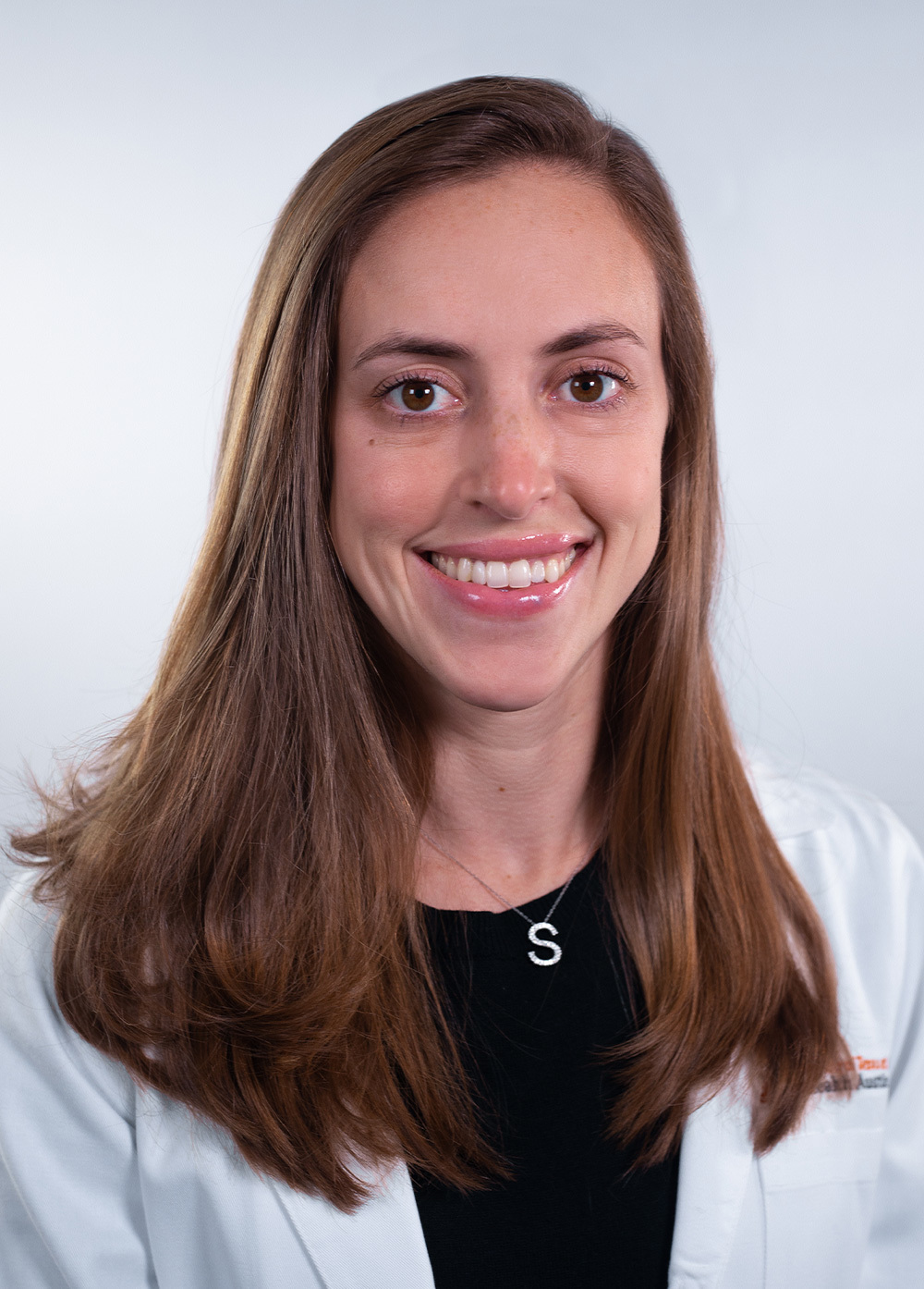 Stephanie Katznelson wearing a white coat and smiling in front of a white backdrop.