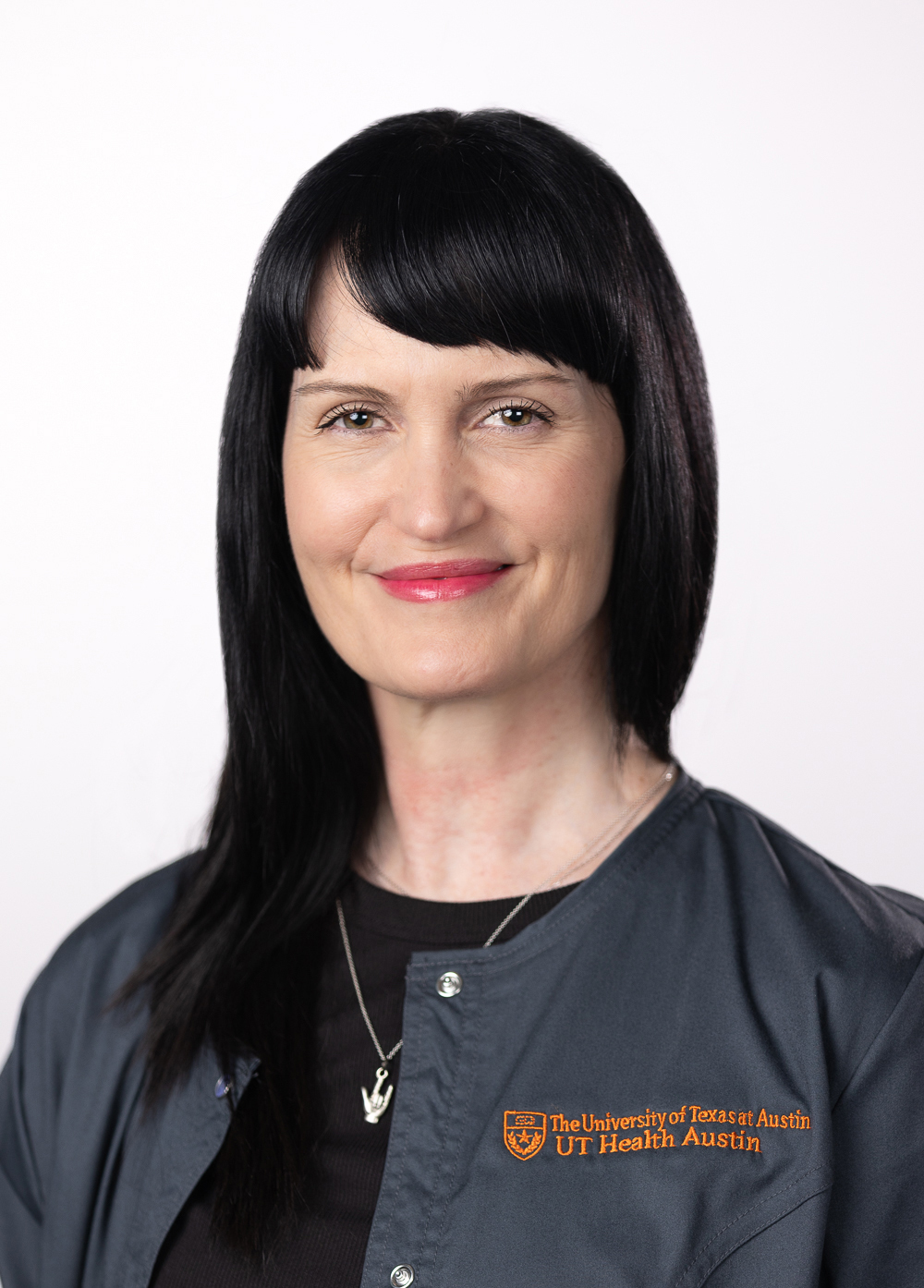 Mammography technician Tracy Seligson wearing a dark jacket embroidered with the UT Health Austin logo and smiling in front of a white backdrop.