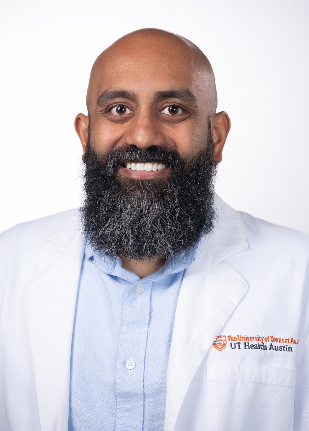 Psychiatrist Vijay Gorrepati, MD, smiling in front of a white backdrop. He is wearing a white coat with an embroidered UT Health Austin logo.