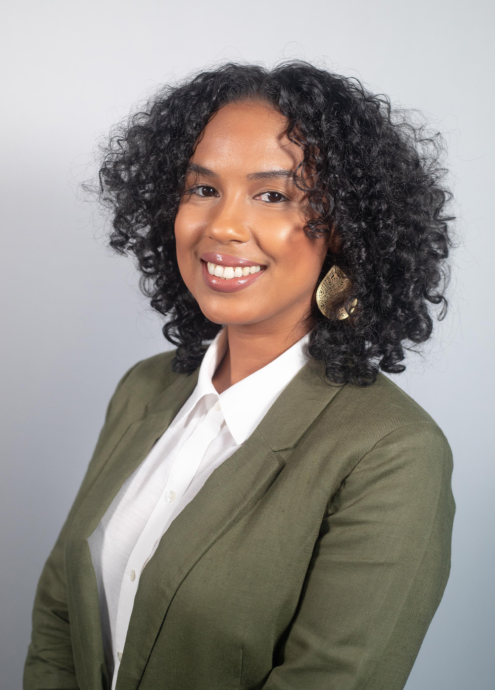 Walkiria "Walki" Raposo wearing a green blazer and white blouse and smiling in front of a white backdrop.