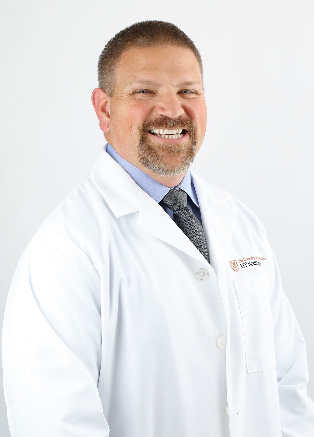 Dr. Karl Koenig wearing a white coat and smiling in front of a white backdrop.