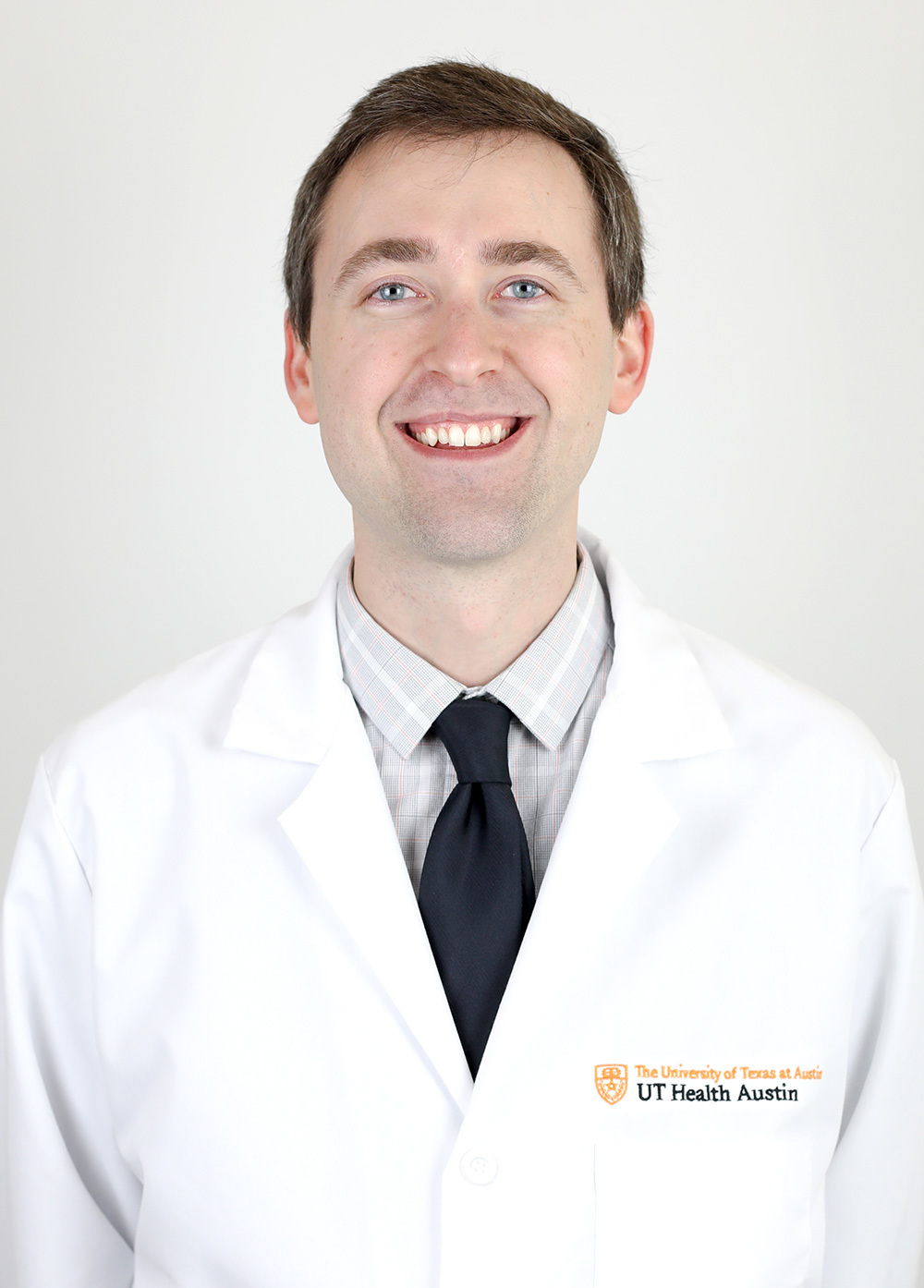 Jeffrey Sanuik wearing a white coat and smiling in front of a white backdrop.