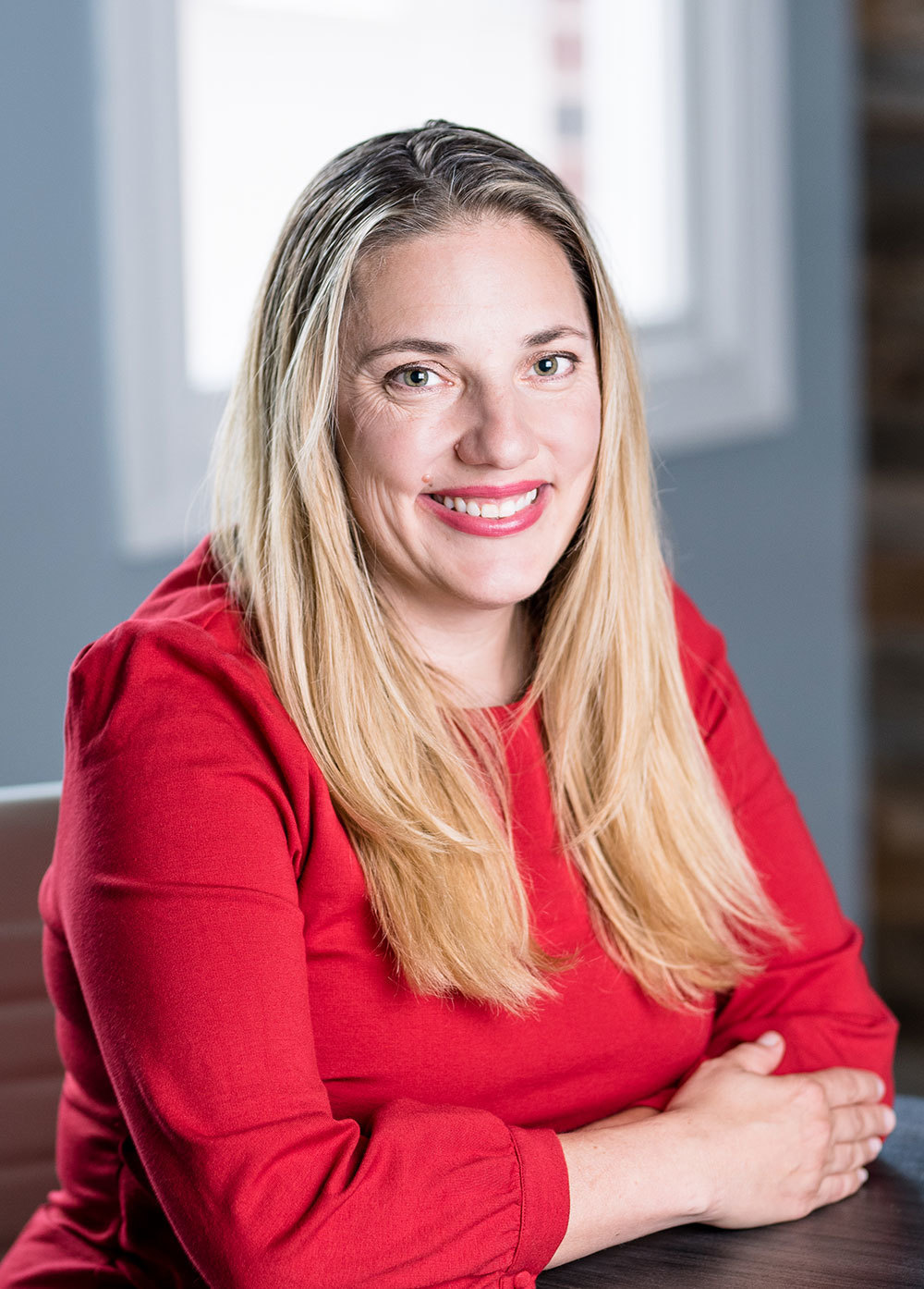 Pediatric cardiologist Chesney Castleberry, MD, seated in front of a window wearing a red blouse and smiling.