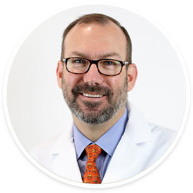 Surgeon F. P. “Tripp” Buckley III, MD, FACS, wearing a white coat and smiling in front of a white backdrop.