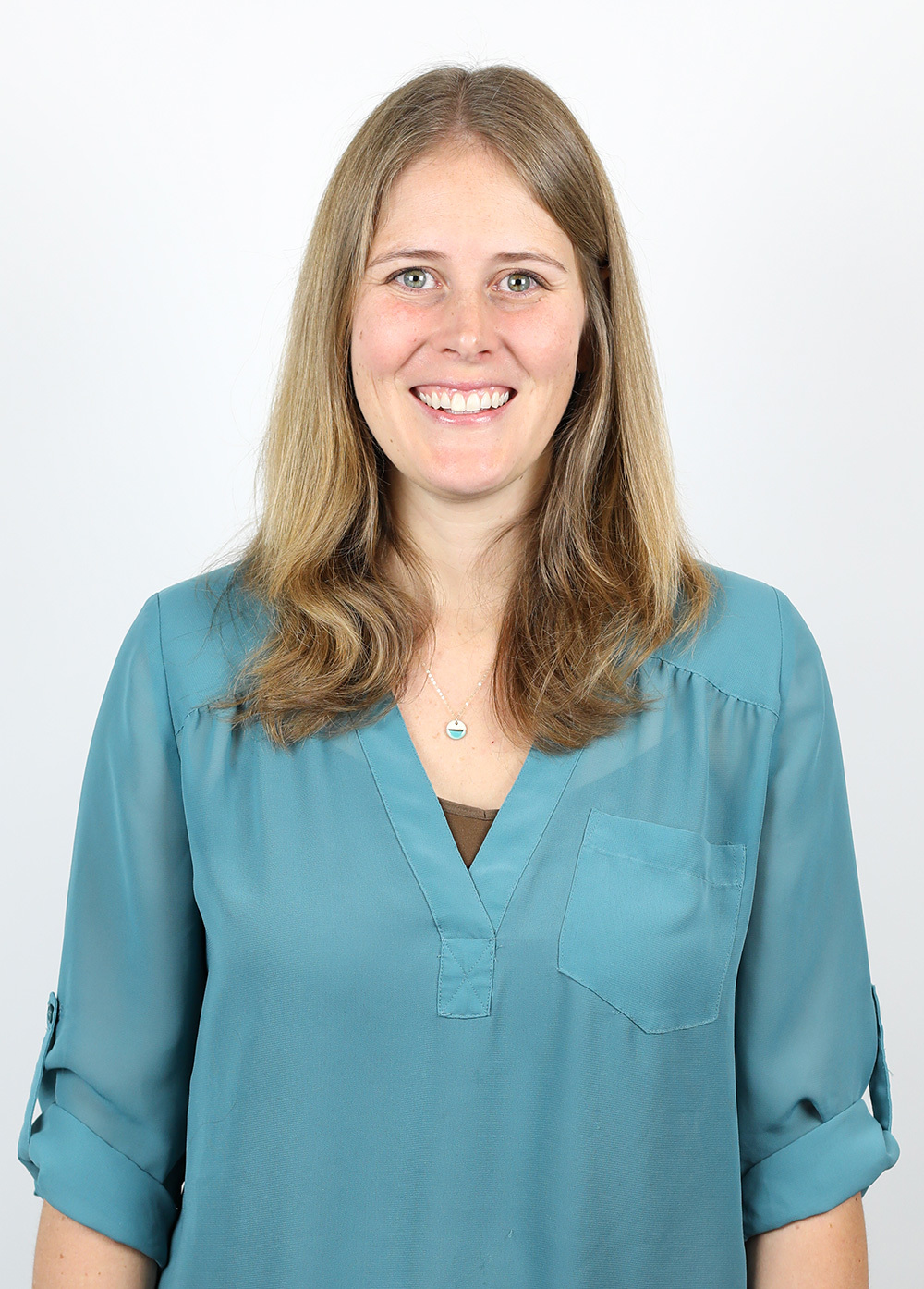 Lindsey Wineholt wearing a blue-green blouse and smiling in front of a white backdrop.