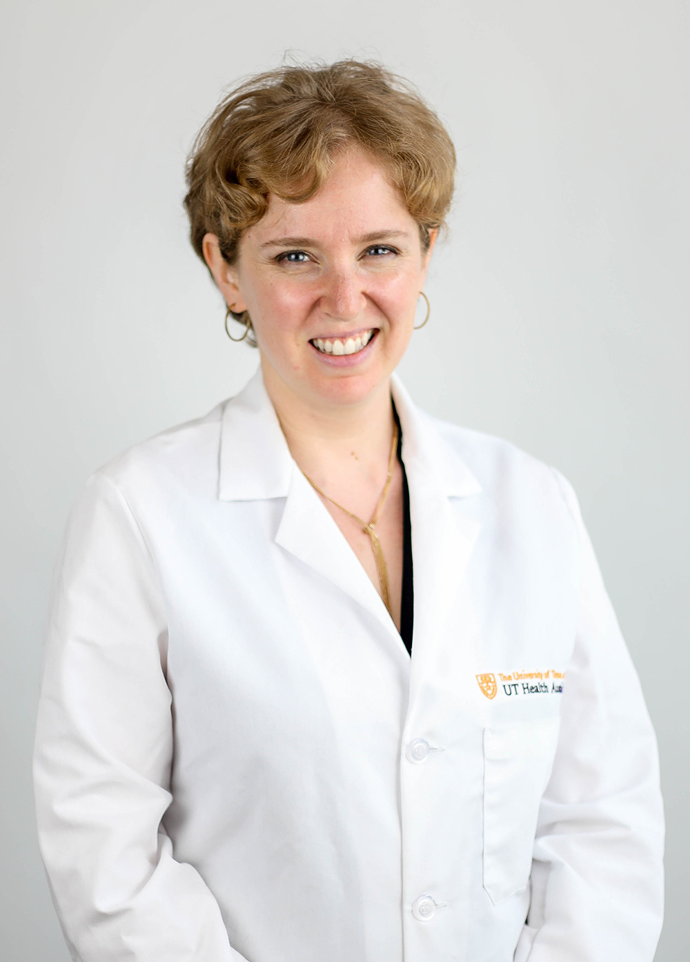 Dr. Esther Melamed wearing a white coat and smiling in front of a white backdrop.